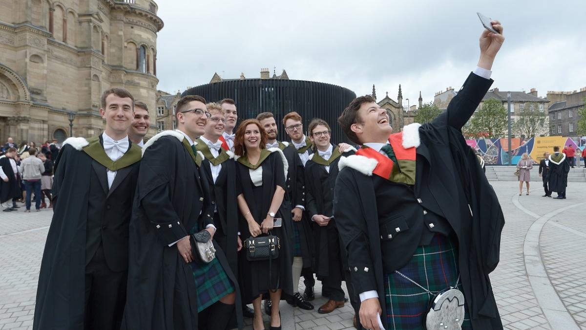 A group of students in graduation robes taking a selfie outside McEwan Hall.