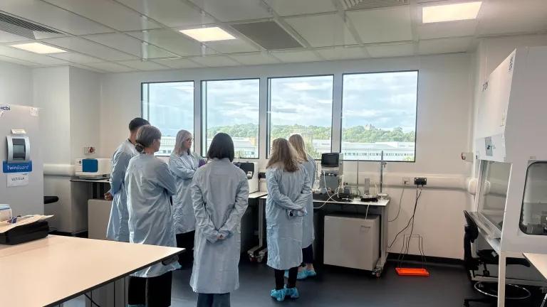 Delegates attending a tour of a GMP-like lab, wearing labcoats