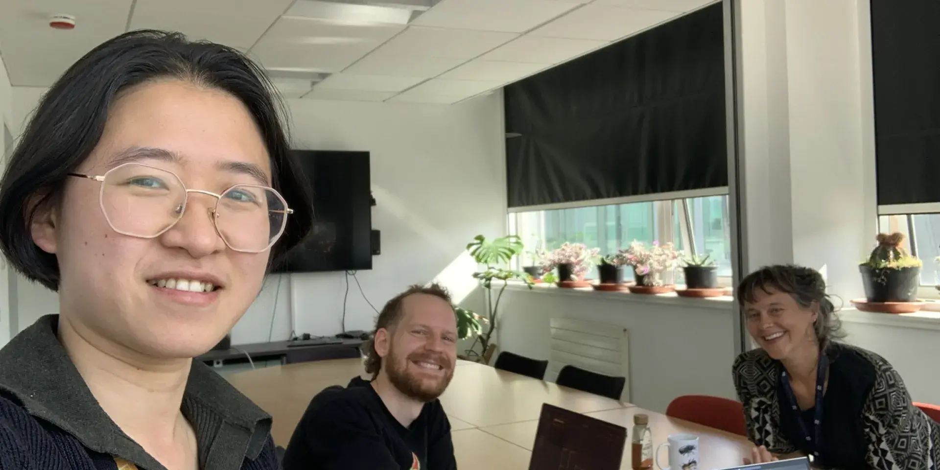 Three people smiling at the camera, two sitting down, one taking a selfie.