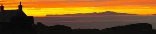 Photo of the Isle of Rum at sunset looking out to sea with a building in the foreground