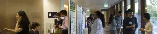 Photo of symposium attendees standing in groups chatting, with drinks and looking at posters