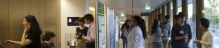 Photo of symposium attendees standing in groups chatting, with drinks and looking at posters