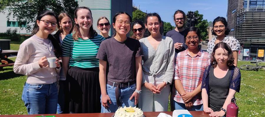 Group photo of lab members outdoors with a table and birthday cake