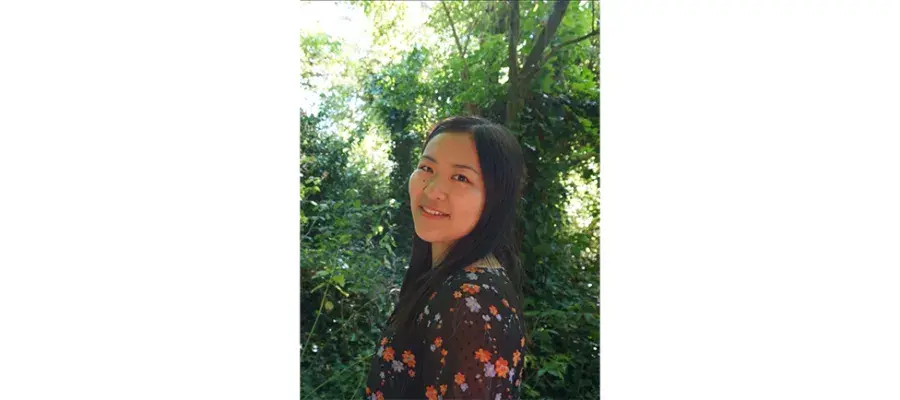 Maxine in the forefront standing and smiling with trees in the background.
