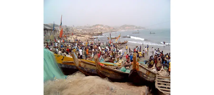 Busy beach in Ghana with many boats in the forefront and background.