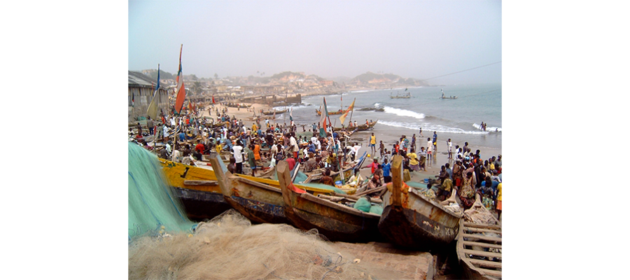Busy beach in Ghana with many boats in the forefront and background.