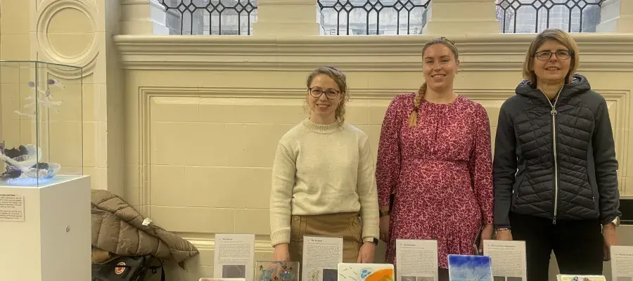 Three contributing artists in the project standing behind a display of tile artworks.