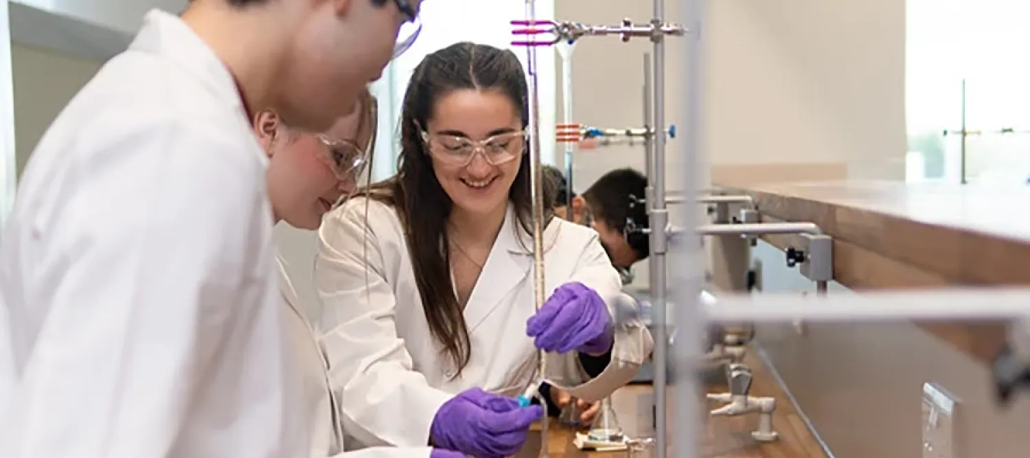 Three people in white lab coats look at scientific instruments whilst one person with purple gloves makes adjustments
