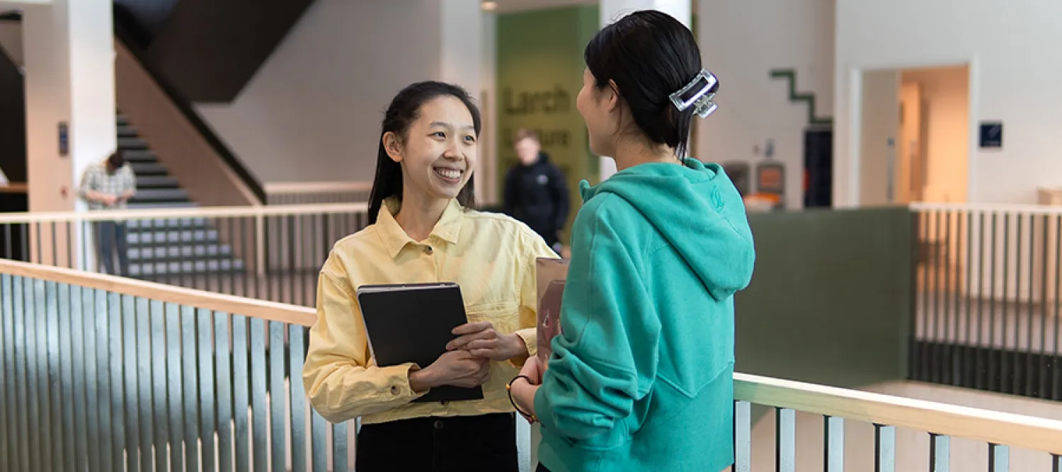 Photo of two students standing chatting on a landing of the Nucleus building
