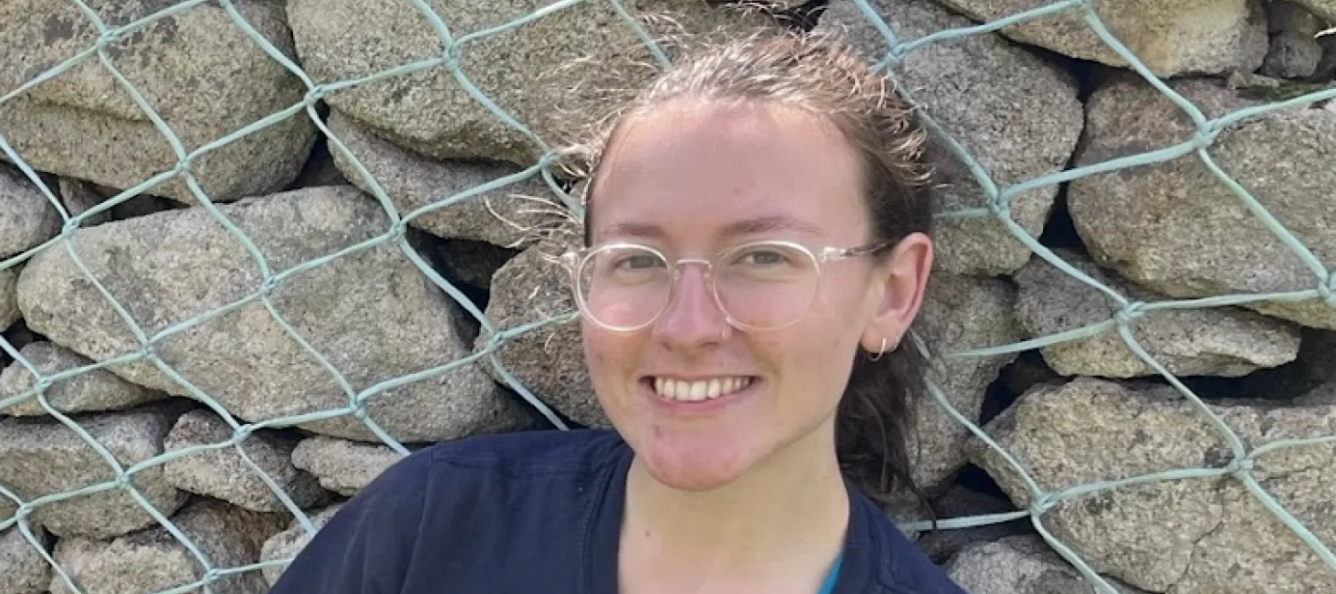 A woman looks at the camera smiling. She has glasses and her hair is up.