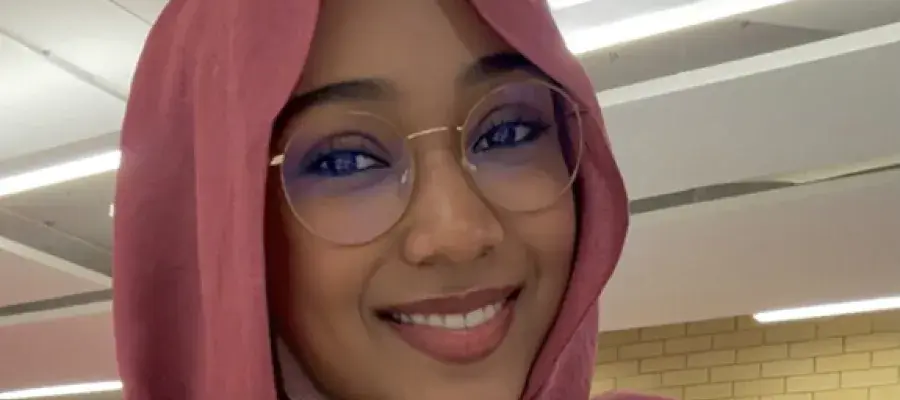 A woman with a head covering and glasses smiling at the camera