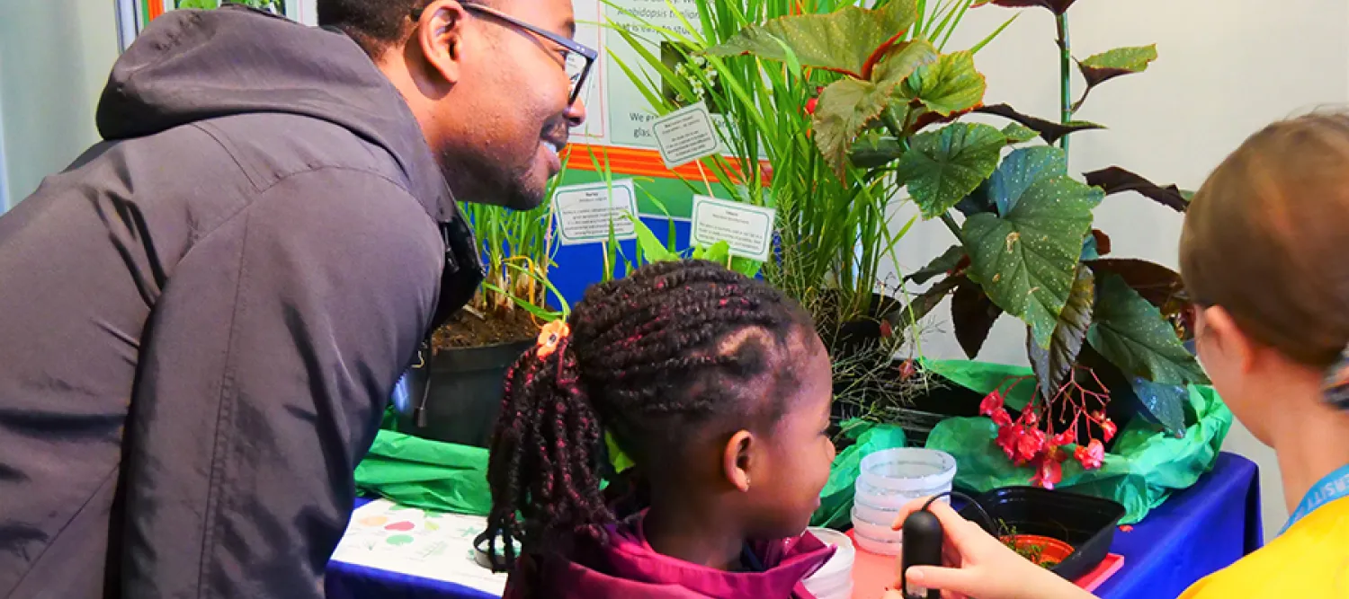 Photo of a parent and child being shown images of a plant through a microscope camera monitor