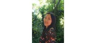 Maxine in the forefront standing and smiling with trees in the background.