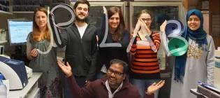 Group photo with the lab members making the letters of 'JP LAB' with their arms, JP crouches in front