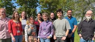 Lab group members posed for photo, standing outside in front of trees and grass