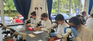 Students in a lab wearing white coats working at benches 