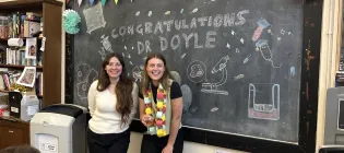 Photo of Rose Doyle and Maddie Moule in front of chalkboard that reads "Congratulations Dr Rose Doyle"