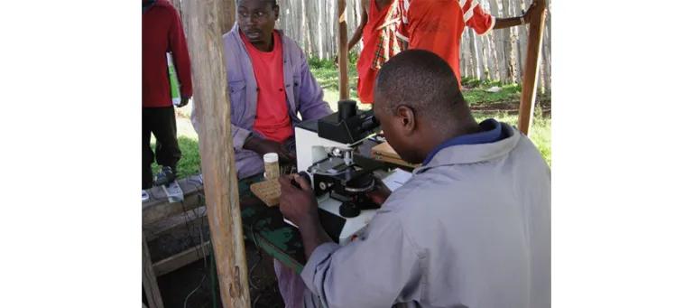 Man looking through a microscope outdoors.