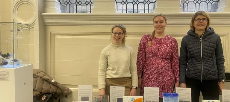 Three contributing artists in the project standing behind a display of tile artworks.