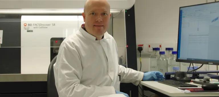Christopher Hall sitting in front of a BD FACSDiscover S8 flow cytometer