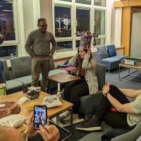 Paula tries on a large, colourful hat whilt surrounded by group members in a seated area