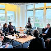 Group members gathered in a seated area with central table which has drinks and nibbles on it