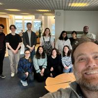 Group photo with lab members in the background and someone standing in front of the camera taking the photo in a selfie style