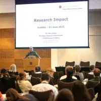 Image of Ismar Haga presenting in front of screen reading Research Impact