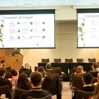 Image of Ismar Haga presenting in front of screen reading Examples of Impact