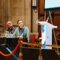 Two people seated at a table with microphones at a conference
