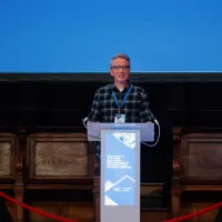 Person speaking at a podium with a blue sign in an auditorium.