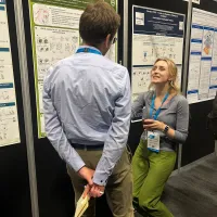Photograph showing two people engaged in discussion at a scientific conference poster session, with multiple research posters displayed.