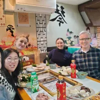 A group dining around a grill table with assorted dishes and drinks, set against traditional Asian decor.