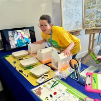 Pedersen of Alex wearing a yellow t-shirt standing behind a table full of props for Edinburgh Science festival
