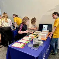 Photo of two group members in yellow t-shirts chatting with members of the public and showing them their props at the Edinburgh Science Festival 