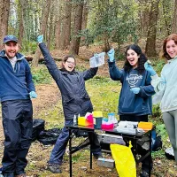 Photo of four fieldworkers standing in a celebratory pose in a wooded area with their samples