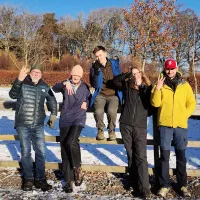Photo of four fieldworkers standing in front of and sitting on a fence, the sun in their faces and a snowy field behind