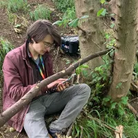 Photo of a fieldwork sitting by a tree and recording data on a handheld device