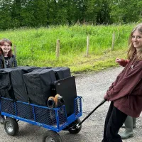 Photo of two fieldworkers one pushing, another pulling, a large cart on a gravely road near a fenced off grassy area
