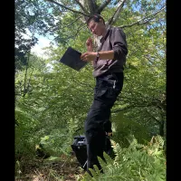 Photo of a fieldworker standing in a wooded area with a clipboard and pen