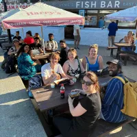 The Hardwick lab and friends sitting at picnic tables enjoying some fish and chips on a sunny day