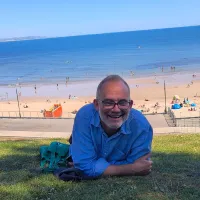 Kevin smiling while sitting in the grass at Lyme Regis