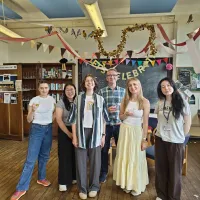 Photograph of six people standing in a decorated room with banners and streamers celebrating an event. 
