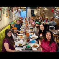 Photo of the lab group sitting round a table in a restaurant with plates of food, some wearing paper crowns