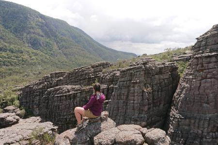 Student sat looking at the view, there are hills and forest and a valley with cliffs.