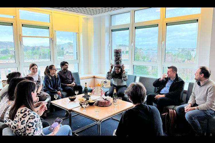 Group members gathered in a seated area with central table which has drinks and nibbles on it