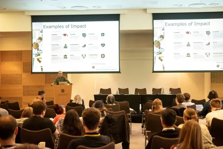 Image of Ismar Haga presenting in front of screen reading Examples of Impact