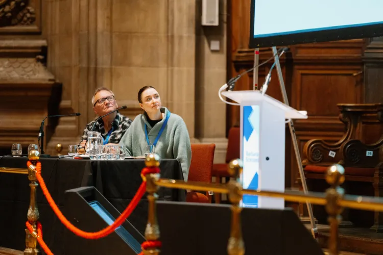 Two people seated at a table with microphones at a conference