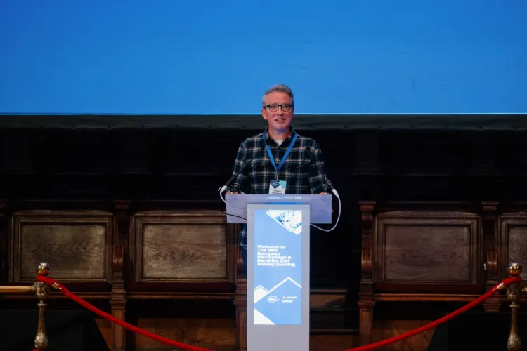 Person speaking at a podium with a blue sign in an auditorium.