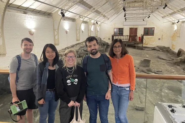 Five people stand infront of fossilised trees at Fossil Grove, Glasgow